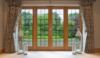 brown french doors with floor length curtains open eitherside and a garden area visible through glazed door panels