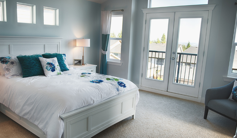 A bedroom space with white french doors (closed) with a Juliette balcony