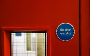 A red fire door with a single glass panel and signage stating: "fire door keep shut"